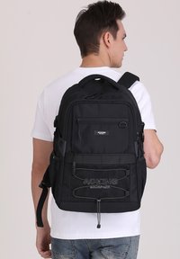 Zaino nero realizzato in tessuto resistente, dotato di più scomparti, tasche con zip e spallacci regolabili; logo ricamato sul fronte.