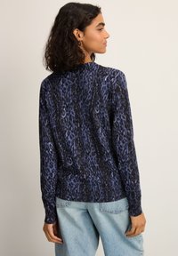 Haut à manches longues violet et noir avec un motif abstrait texturé, un col rond, des poignets côtelés et une coupe légèrement décontractée.