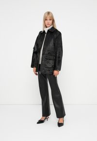 Mustast kunstkarvast jakist, millel on tõmblukuga sulgemine, kaks esipakki, millele on lisatud mustad nahkpüksid ja mustad teravatippe kingad.