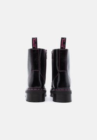 Μαύρα γυαλιστερά αρβυλάκια πλατφόρμας με ροζ ραφές και ταινίες έλξης που γράφουν "WITH SOLES BOUNCING", από πίσω, σε λευκό φόντο.