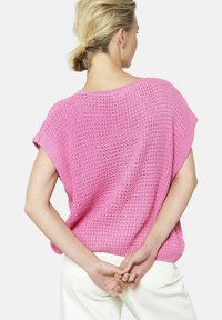 Rozā adīta džemperis ar brīvu piegriezumu, īsām piedurknēm un teksturētu dizainu, parādīts no aizmugures. Saskaņots ar baltām biksēm.