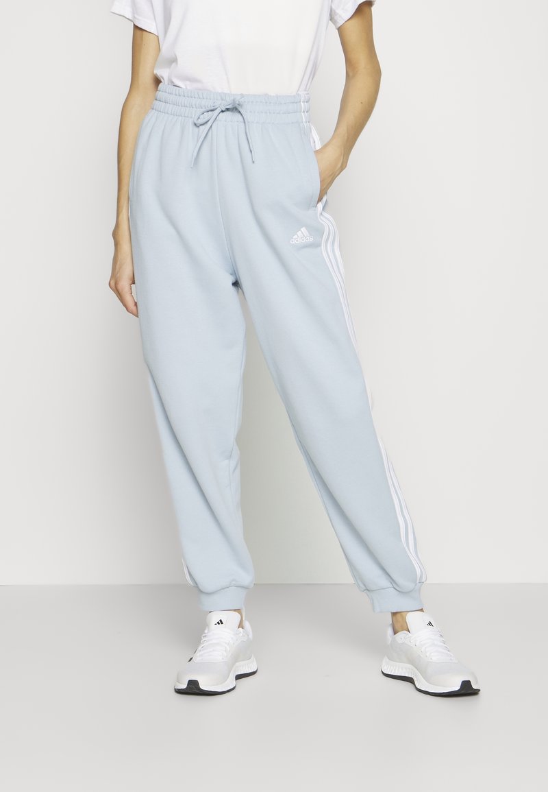 Pantalons de jogging bleu clair avec taille élastique, cordon de serrage, poches latérales et accents blancs à trois bandes. Le matériau semble doux et lisse.