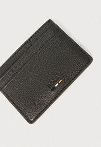 Czarny skórzany futerał na karty z teksturowaną powierzchnią, czterema przegródkami na karty oraz wytłoczonym logo z kolorowymi akcentami w czerni, bieli i brązie.