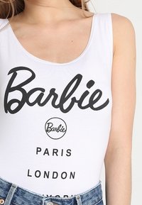 Bílé tílko s černým logem "Barbie" a názvy měst: Paříž, Londýn a New York. Materiál je hladký a pružný.