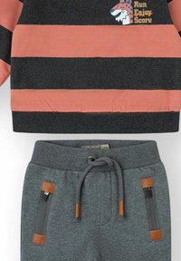 Conjunto infantil con una camiseta de manga larga a rayas naranja y negra con un tigre de dibujos animados y texto, combinado con pantalones grises con cordón y bolsillos con cremallera.