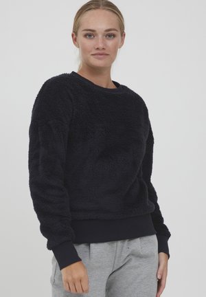 Navy blue fleece sweatshirt with a soft, textured finish, crew neckline, and ribbed cuffs, paired with light gray sweatpants.