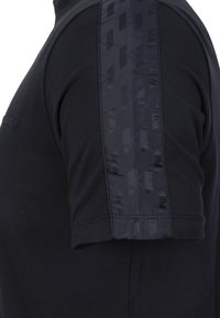 Camicia nera a maniche corte con un accento lucido e decorato sulla manica, caratterizzata da tessuto liscio e design aderente.