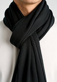 Zwarte gebreide sjaal met een gestructureerd patroon, gedrapeerd rond de hals. Glad weefsel contrasteert met het effen witte overhemd eronder.
