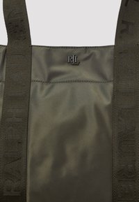 Olívazöld textil táska sima felülettel, logós hardverrel és széles fogantyúkkal, melyeken a "RALPH LAUREN" felirat található.