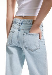 Vaqueros de mezclilla azul claro con corte relajado, que cuentan con dos bolsillos traseros y una etiqueta de cuero en la cinturilla. Textura suave, diseño casual.