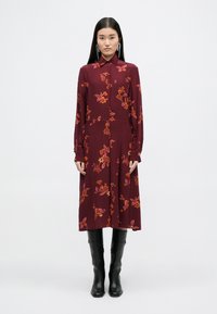 Μαραoon μακρυμάνικο φόρεμα με λουλουδάτα σχέδια σε κόκκινο, πορτοκαλί και ροζ. Διαθέτει γιακά και μπροστινό κλείσιμο με κουμπιά. Φοριέται με μαύρες μπότες μέχρι το γόνατο.