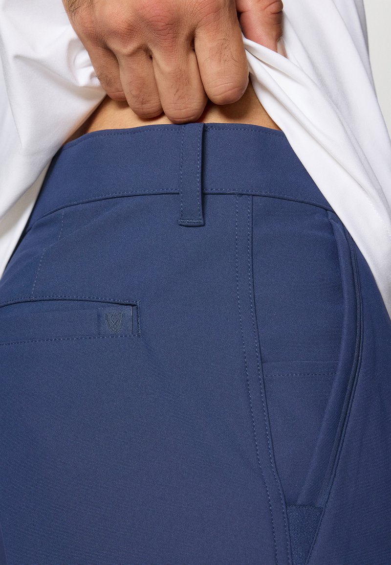 Pantalon bleu marine en tissu lisse, avec une ceinture cousue, un détail de poche arrière et un logo subtil à l'arrière.