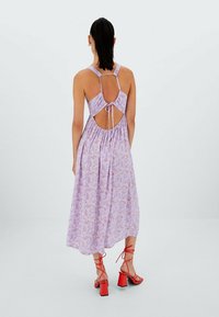 Robe maxi florale violette avec des fines bretelles, un dos ouvert et une taille froncée. Associée à des sandales à talons blocs rouges.