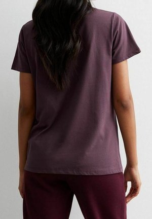 Fioletowy, bawełniany t-shirt z krótkim rękawem i okrągłym dekoltem; gładka faktura, luźny krój i przeszywany brzeg. Noszony wraz z pasującymi spodniami.