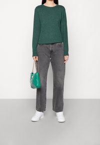 Green knitted sweater, gray straight-leg jeans, white sneakers, and a green handbag with a chain shoulder strap.