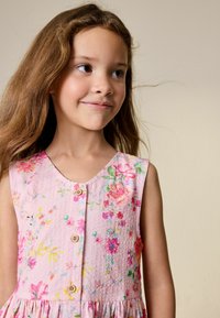 Vestido floral rosa con tela texturizada, escote en V y botones de madera. Presenta patrones de flores coloridas y detalle de falda fruncida.