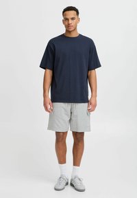Navy Baumwollt-Shirt mit kurzen Ärmeln, kombiniert mit hellgrauen Cargo-Shorts, die über zwei Fronttaschen und einen elastischen Bund verfügen. Graue Sneakers.