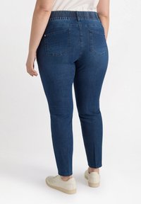 Jeans de mezclilla de color azul oscuro, con una cinturilla elástica, forma de pierna ajustada y dos bolsillos traseros. Textura suave y diseño casual.