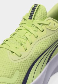 Neon sárga Puma sportcipő hálós felsőrésszel, hozzáillő fűzőkkel és fekete csíkkal az oldalsó fehér talp mentén.