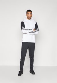 White hoodie with black sleeves and three white stripes, paired with black sweatpants featuring side stripes and black athletic shoes.