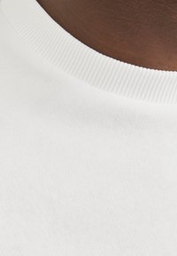Witte katoenen t-shirt close-up, met een gestructureerde ribbenhals en een gladde stofoppervlak. Geen patronen of extra details zichtbaar.