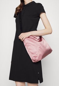 Robe polo noire à manches courtes, avec patte de boutonnage et détail de logo. Tenue d'un grand sac en satin rose doux avec un haut froncé.