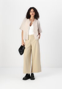 Cardigan rosa chiaro con maniche corte e chiusura a bottoni; canotta bianca; pantaloni larghi beige; borsa nera; scarpe nere con piattaforma.