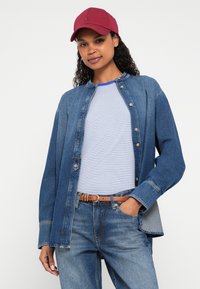 Πουκάμισο από τζιν με κουμπιά και γιακά, μπλε και φωτεινή μπλε ριγέ φανελάκι από μέσα και ανοιχτό μπλε τζιν παντελόνι. Μπορντό καπέλο και καφέ ζώνη.