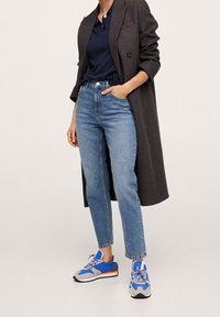 Niebieskie dżinsy z wysokim stanem i prostymi nogawkami, zestawione z granatową koszulką polo i ciemnym płaszczem w kratę, oraz niebiesko-szare sneakersy.