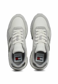 Zapatillas grises y blancas con un upper texturizado, que cuentan con cordones, una suela negra y una etiqueta de logo en el interior del zapato.