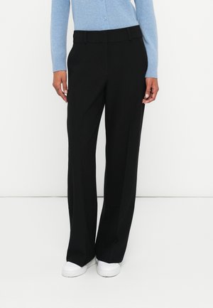 Sorte brede bukser med en glat overflade, flad front og pressefolder. Båret med en lyseblå knap-up cardigan og hvide sneakers.
