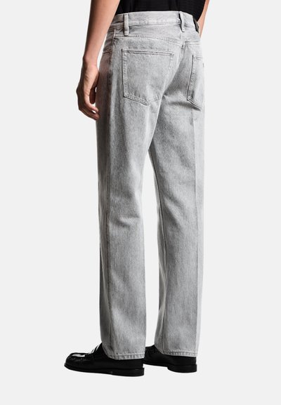 Jeans in denim grigio chiaro con vestibilità rilassata, cuciture visibili, due tasche posteriori e un classico girovita, abbinati a scarpe nere.