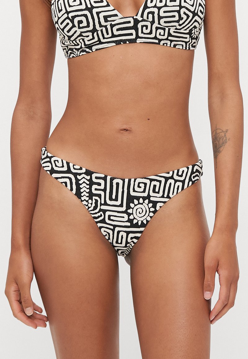 Bikini à motifs noir et blanc, avec des designs géométriques et un tissu texturé. Le bas est à taille basse avec des bandes latérales étroites.
