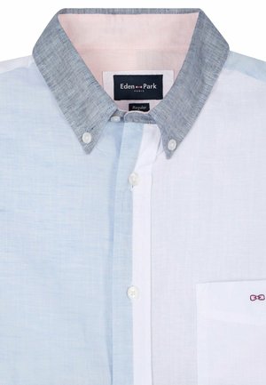 Chemise boutonnée avec panneaux bleu clair et blanc, col boutonné gris, boutons blancs et petit logo nœud rose sur la poche poitrine.