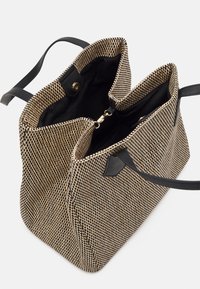 Sac cabas texturé à motif à carreaux noir et beige, comprenant deux compartiments, intérieur noir et bretelles en cuir noir.