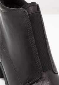 Botín negro de piel con panel lateral elástico, textura suave y detalles de costura visibles. Silueta moderna y estilizada con un tacón bajo.