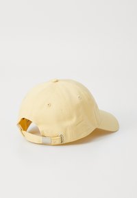 Casquette de baseball en coton jaune avec une visière courbée, une sangle réglable à l'arrière et une texture lisse. Comprend un détail de boucle en métal.