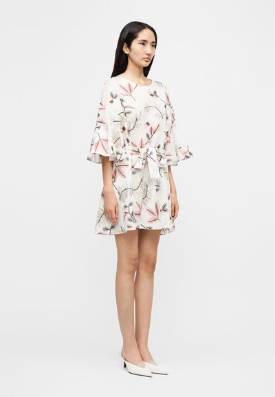 Φόρεμα με λουλουδάτο μοτίβο σε ελαφρύ ύφασμα, με κοντά μανίκια με βολάν, ζώνη στη μέση και φουσκωτή τελική ραφή. Φορεμένο με λευκά παπούτσια με τακούνι.