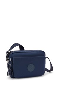 Námořnická crossbody taška vyrobená z nylonu, s uzávěrem na zip, přední kapsou a kruhovou nášivkou s logem. Obsahuje dekorační klíčenku.