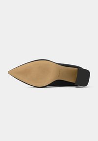 Scarpa nera con tacco alto, punta affilata, tomaia testurizzata e suola beige liscia con un motivo rigato e logo.