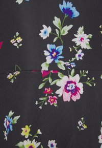Tejido floral con un fondo negro y flores coloridas en rosa, azul, blanco y amarillo, que muestra una superficie texturizada.