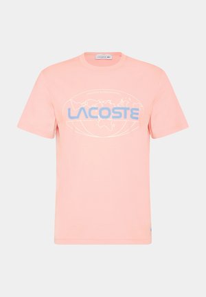 Camiseta de algodón color rosa claro con un gráfico de un globo azul y el texto "LACOSTE INTERNATIONAL", cuello redondo clásico y mangas cortas.