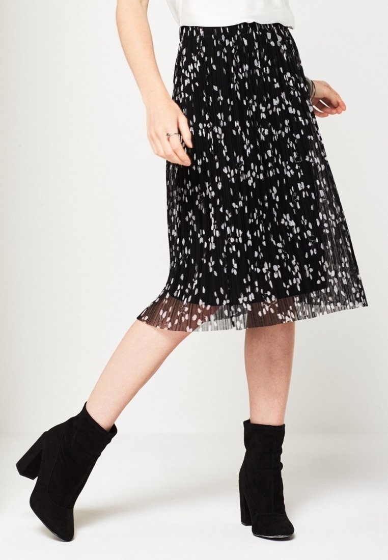 Černá plisovaná sukně s bílým květinovým vzorem, délka po lýtka. Kombinována s černými kotníkovými botami s blokovým podpatkem.