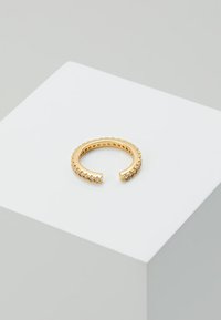 Anillo abierto en tono dorado con una banda texturizada y una fila de cristales claros a lo largo de un lado, con un acabado liso y un diseño minimalista.