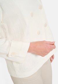 Lätt, off-white linnejacka med dubbelknäppning och fyra runda knappar. Har en avslappnad passform och strukturerade manschetter.