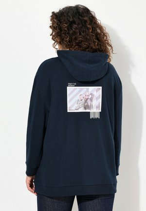 Hoodie bleu marine avec une coupe ample, arborant un grand imprimé graphique au dos représentant deux personnes et du texte, ainsi qu'un détail de code-barres en bas.