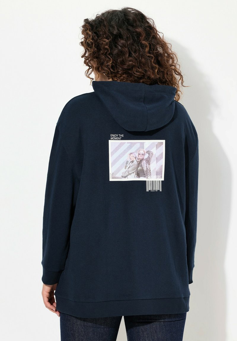 Felpa blu navy con vestibilità ampia, caratterizzata da una grande stampa grafica sul retro che raffigura due persone e del testo, con un dettaglio a codice a barre nella parte inferiore.