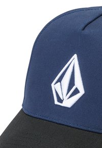 Casquette de baseball bleu marine avec un visière noire, arborant un logo géométrique blanc à l'avant. Conçue en tissu avec une finition texturée.