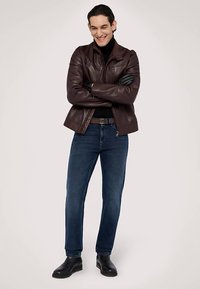 Chaqueta de cuero marrón, cuello alto negro, vaqueros azules, botines negros. La chaqueta cuenta con cierre de cremallera y acabado texturizado.