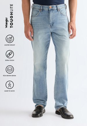 Férfi világoskék egyenes szabású farmernadrágban és fekete cipőben, ikonokkal kiemelve a könnyű súlyt, extra tartósságot, technológiailag fejlett farmert és a mozgás szabadságát biztosító jellemzőket.